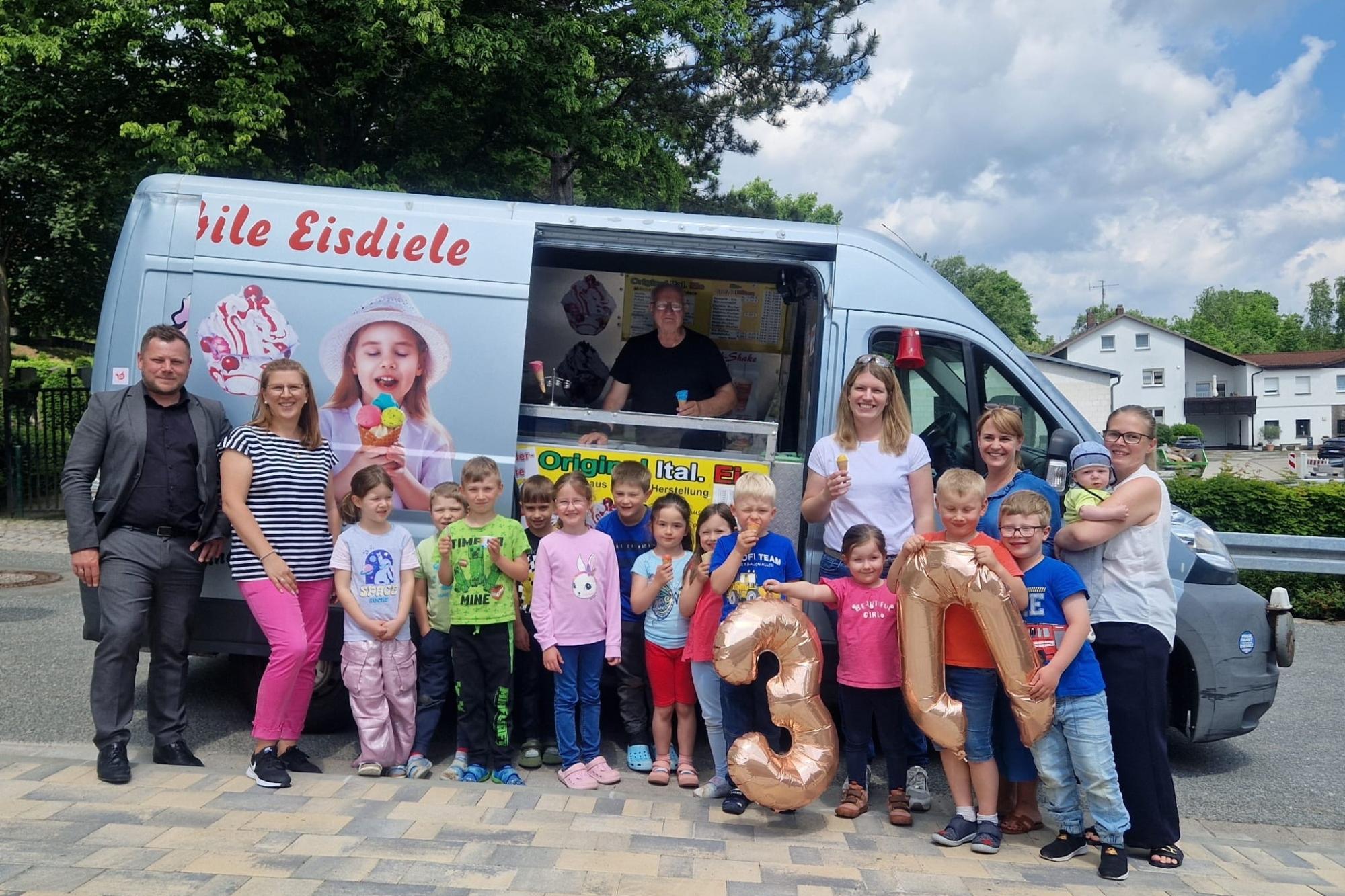 Kinder und Erwachsene stehen vor dem Eiswagen und essen Eis