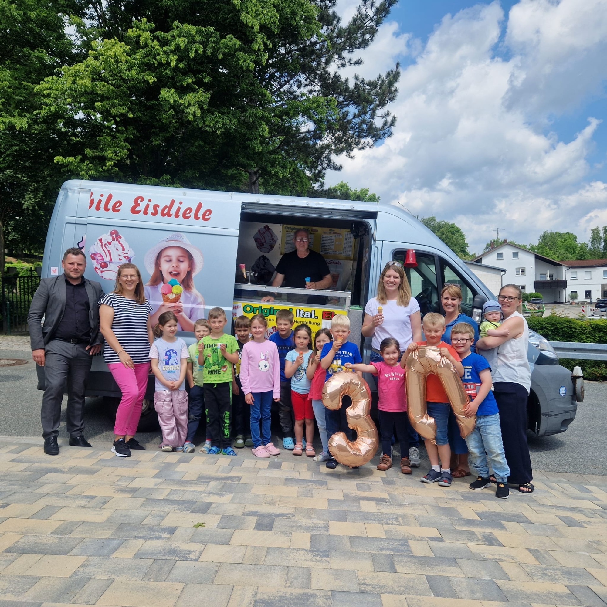 Kinder und Erwachsene stehen vor dem Eiswagen und essen Eis